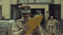 a police officer is holding a yellow folder in front of a sign that says ' central jail - kalyalaya '