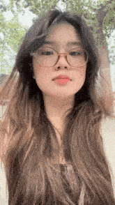 a young woman with long hair and glasses is taking a selfie .