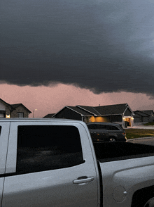 a white truck is parked in front of a house with a storm in the background