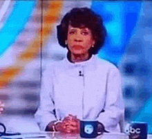 a woman is sitting at a table with her hands folded in front of a microphone on a television .