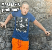 a young boy wearing a blue shirt and orange shorts is standing in front of a stone wall with the caption masz jakis problem