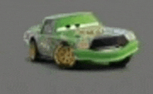 a green toy car from the movie cars is sitting on a grey surface .