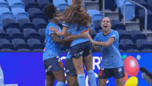 a group of female soccer players are hugging each other in front of a sign that says the lot off .