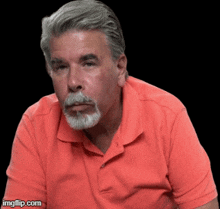 a man with gray hair and a beard wearing an orange polo shirt