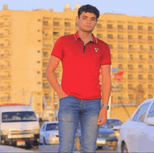 a young man wearing a red polo shirt and blue jeans is standing in front of a building .