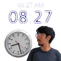 a man wearing glasses stands in front of a clock that says 08:27 am