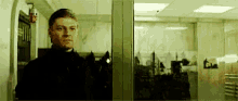 a man in a black suit is standing in front of a glass door .