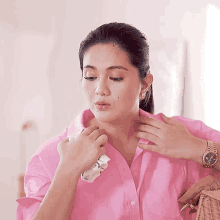 a woman wearing a pink shirt and a watch is adjusting her shirt collar