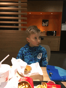 a young boy sits at a mcdonald 's table with a hamburger and fries