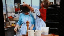 a man and a woman are standing in a kitchen and the man is pouring something into the woman 's head