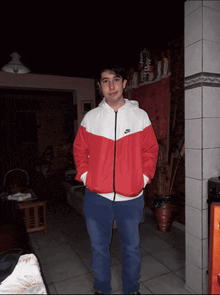 a man in a red and white nike jacket stands in a dark room