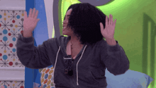 a woman in a grey hoodie is waving her arms in the air
