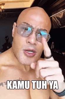 a bald man wearing glasses is pointing at the camera with the words kamu tuh ya above him