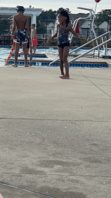 a little girl in a swimsuit is standing on the edge of a swimming pool