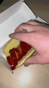 a person with a tattoo on their finger is holding a hot dog with ketchup