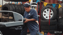 a man is working on a car in front of a stack of tires and a sign that says netflix on it