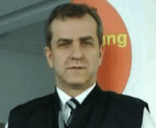 a man in a suit and tie is standing in front of an orange circle that says ing