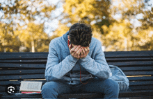 a man sits on a bench with his head in his hands and a book in front of him