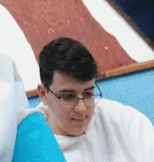 a young man wearing glasses and a white shirt looks down