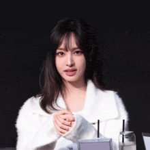 a woman wearing a white sweater holds her hands together in front of a bottle with a straw on it