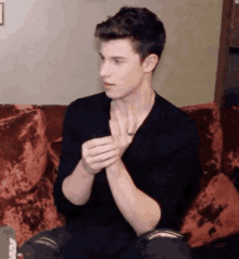 a young man is sitting on a couch and clapping his hands