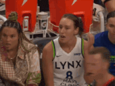 a woman wearing a lynx jersey sits in the stands with other women
