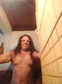 a shirtless man with long hair and glasses smiles