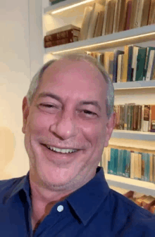 a man in a blue shirt is smiling in front of a bookshelf filled with books