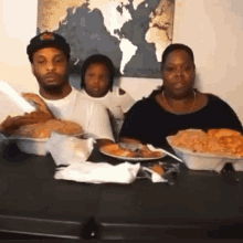 a family is sitting at a table with plates of food and a map of the world behind them .