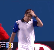 a man in a white and blue polo shirt stands in front of a scoreboard that says match point on it