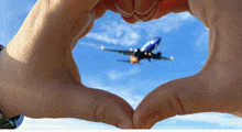 a person making a heart shape with their fingers while a plane is flying in the background