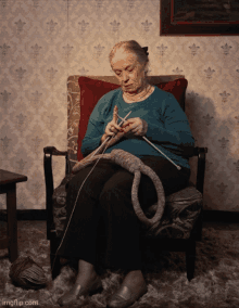 an older woman is knitting while sitting in a chair with a red pillow