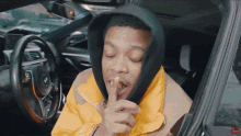 a man wearing a hooded jacket is sitting in a car with his eyes closed