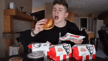 a man is eating a hamburger from a box that says kfc on it