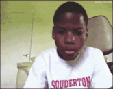 a young boy wearing a souderton shirt is making a funny face