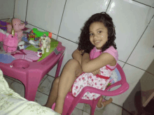 a little girl is sitting in a pink chair in front of a pink table