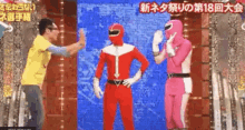 a man in a yellow shirt is standing next to two power rangers in red and pink costumes on a stage .