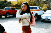 a woman with dreadlocks and a pink backpack is standing in a parking lot with cars parked behind her .