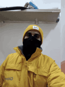 a man wearing a yellow jacket and a yellow beanie has a black face mask on