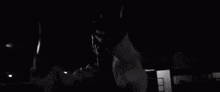 a man in a white hoodie is standing in the dark holding a knife .