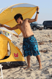 a shirtless man stands in front of a yellow bestway tent on the beach