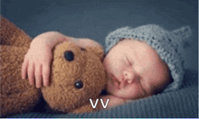 a baby wearing a knitted hat is sleeping with a teddy bear with the letter vv below it