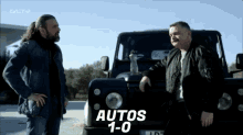 two men are standing in front of a car that says autos 1.0 on the screen