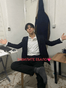 a man in a suit sits on a chair with his arms outstretched in front of a desk with a keyboard and mouse