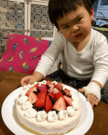 a little boy is sitting in front of a cake with strawberries and blueberries on it