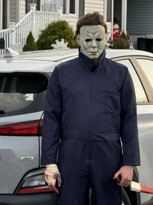 a man dressed as michael myers holds a bloody knife in front of a tesla model 3