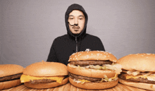 a man wearing a nike hoodie is surrounded by hamburgers on a table