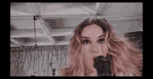 a close up of a woman singing into a microphone with a ceiling behind her