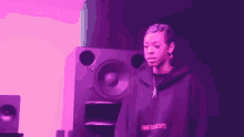 a woman in a purple hoodie stands in front of a speaker