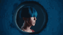 a man with blue hair and a pearl necklace is looking through a hole in a wall .